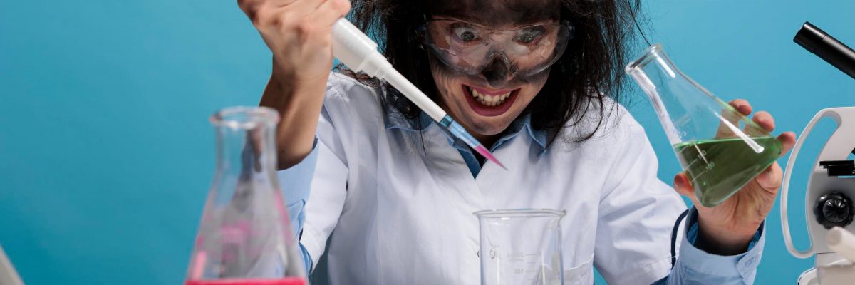 crazy-mad-scientist-mixing-liquid-substances-while-grinning-dreadful-and-sitting-at-desk-on-blue-background-foolish-silly-lab-worker-with-pipette-and-glass-jar-mixing-chemical-compounds-studio-shot